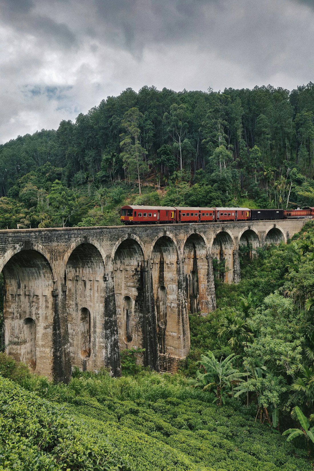 A red train crossing the Nine Arches Bridge in the jungle near Ella