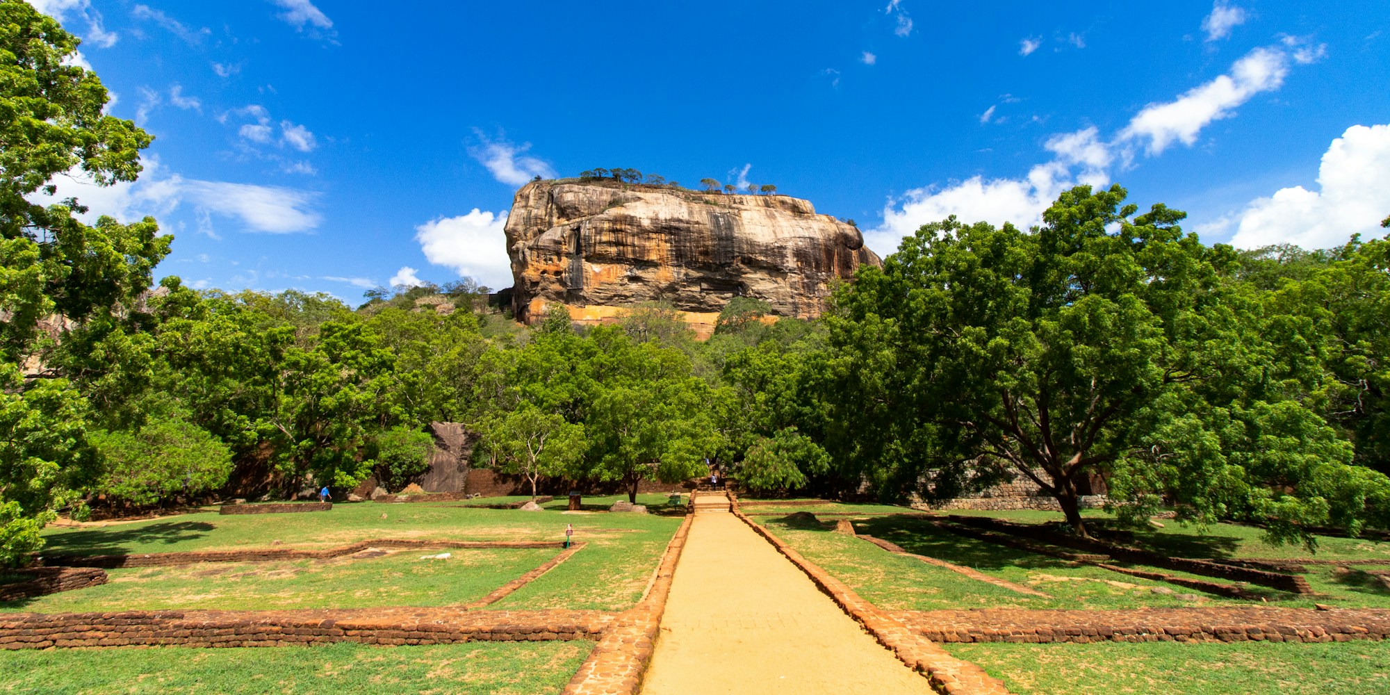The walkway through the water gardens leading up to Sigiriya rock fortress under a clear blue sky