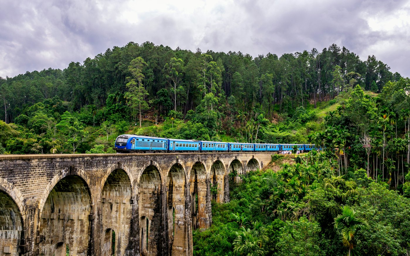 Blue train crossing the Nine Arches Bridge above tea country near Ella